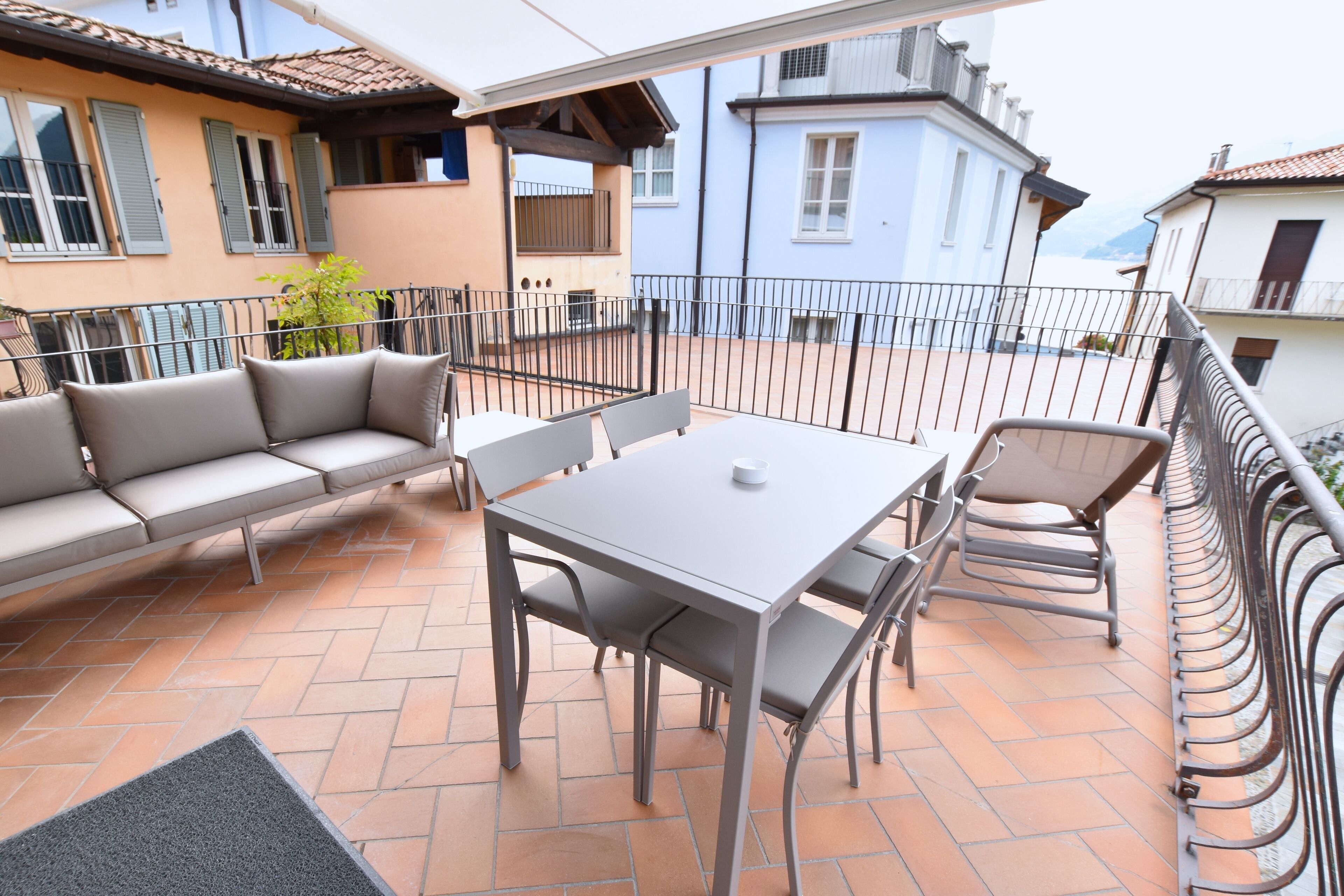 A terrace with a sofa, table, and chairs, surrounded by a metal railing.