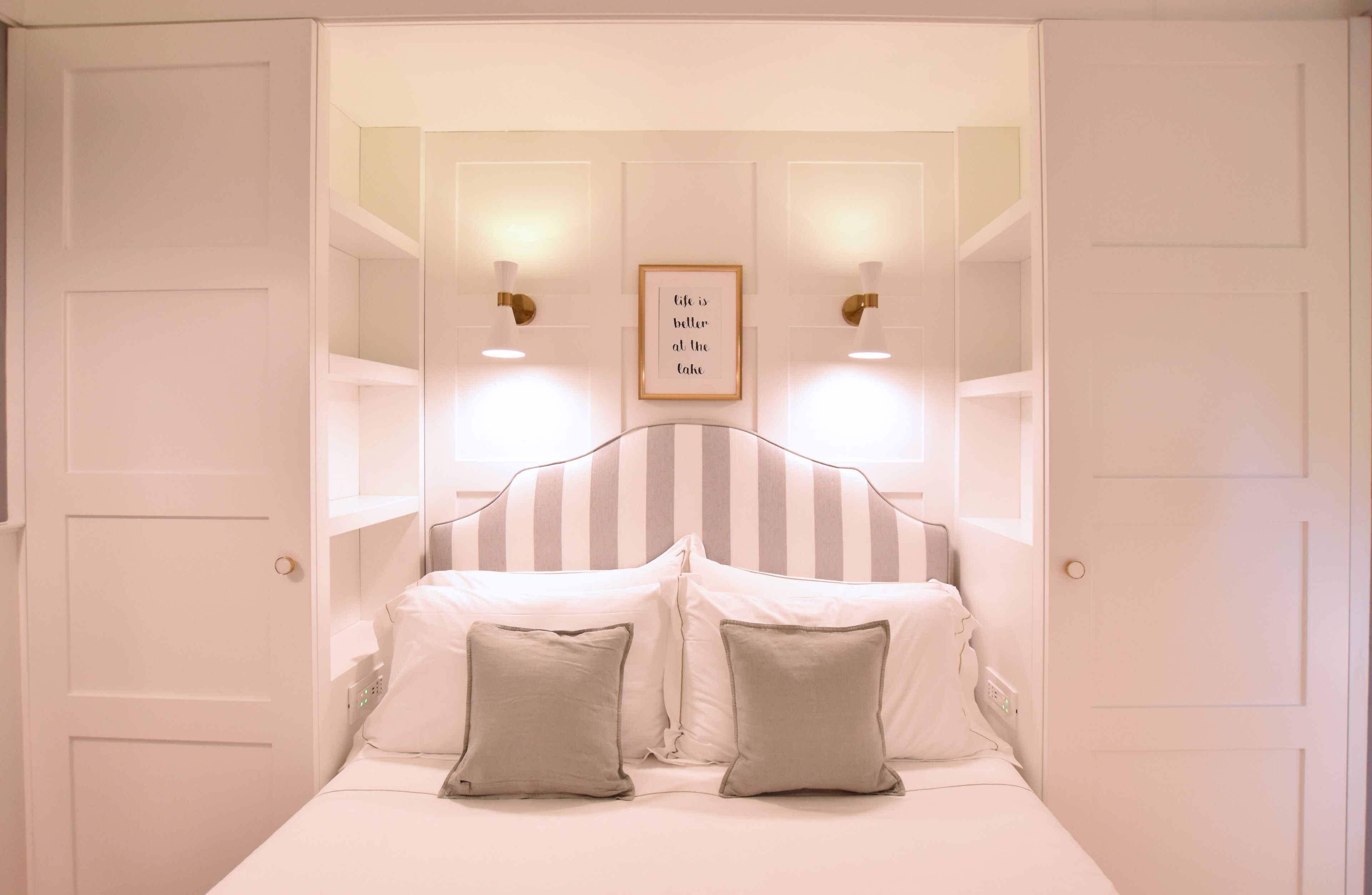 A bedroom with a bed, two bedside lamps, and a framed quote on the wall.