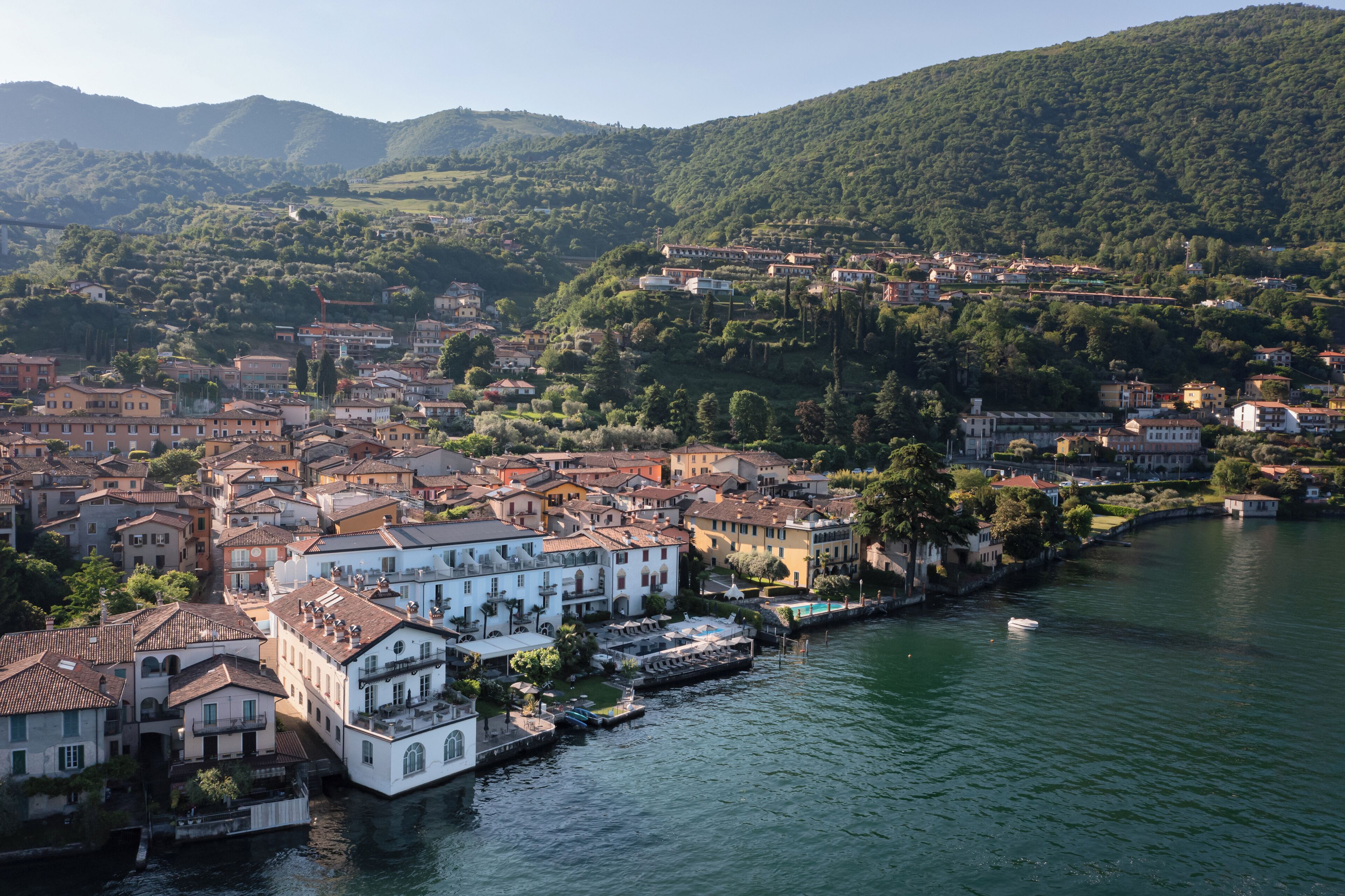Une ville riveraine, avec des bâtiments qui bordent le cours d’eau, un quai et une colline en arrière-plan.
