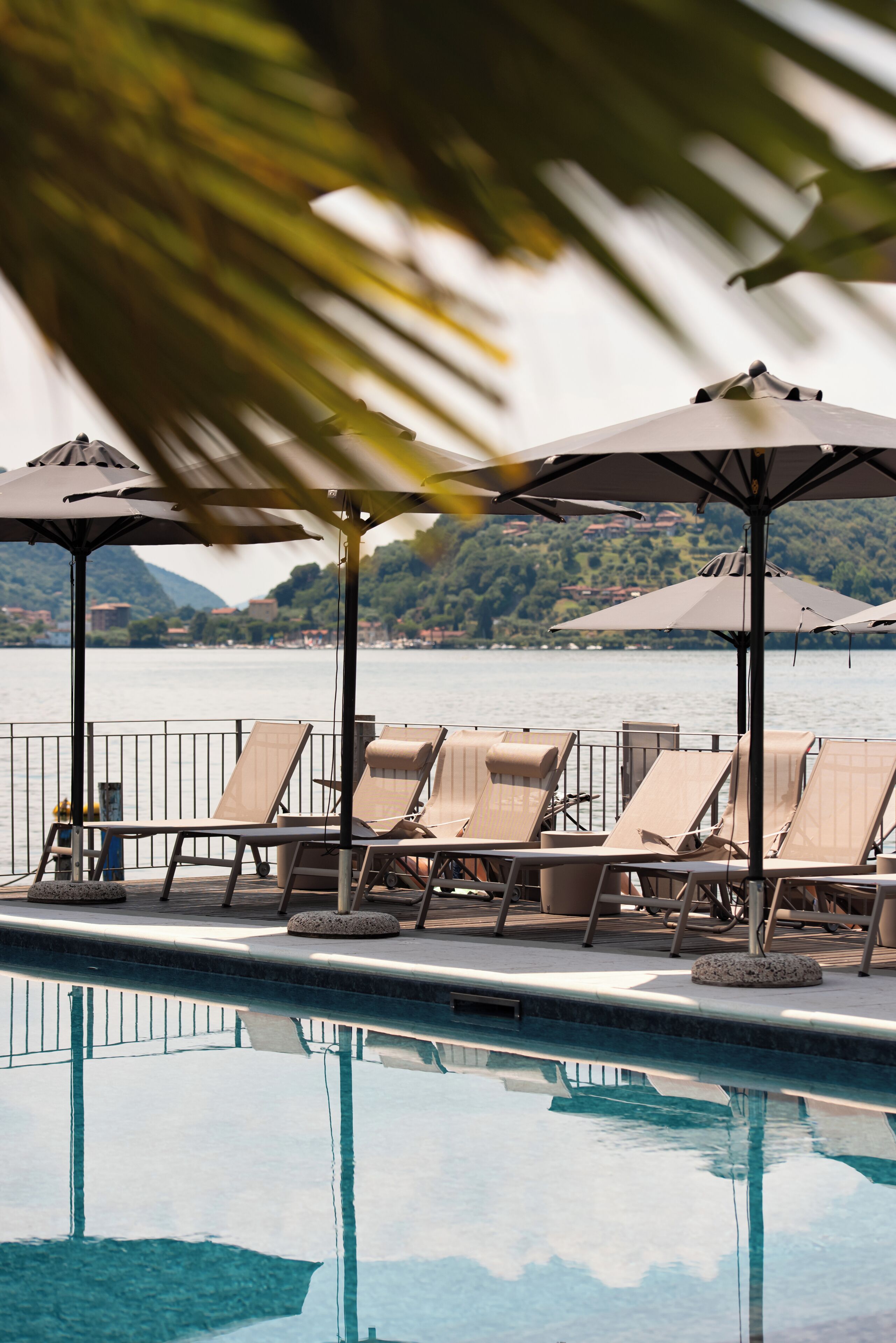 Un espace aménagé au bord de la piscine, avec des chaises longues et des parasols, offrant une vue dégagée sur l’eau et un paysage montagneux en toile de fond.