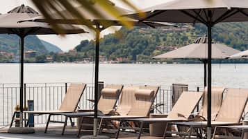 A poolside area with lounge chairs and umbrellas, a clear view of the water, and a mountainous backdrop.