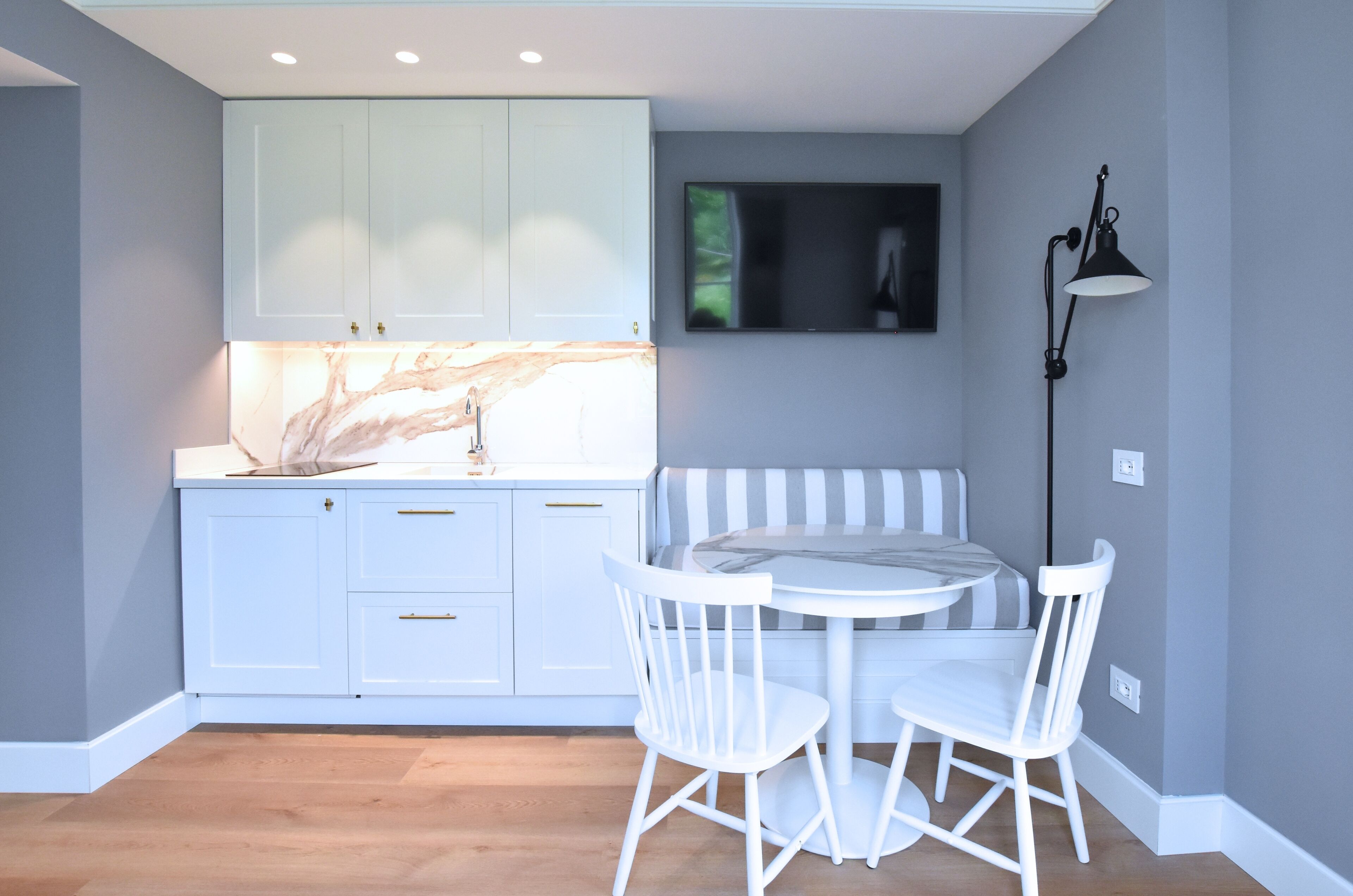 Una cocina moderna con armarios blancos, encimera de mármol, pileta integrada y una mesa de comedor redonda con dos sillas blancas.