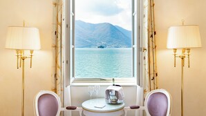 Una habitación con vistas a un lago y montañas, una mesa con una botella y vasos, y dos lámparas.
