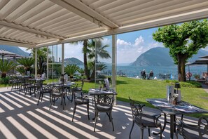 An outdoor dining area with tables and chairs, overlooking a body of water and mountains.