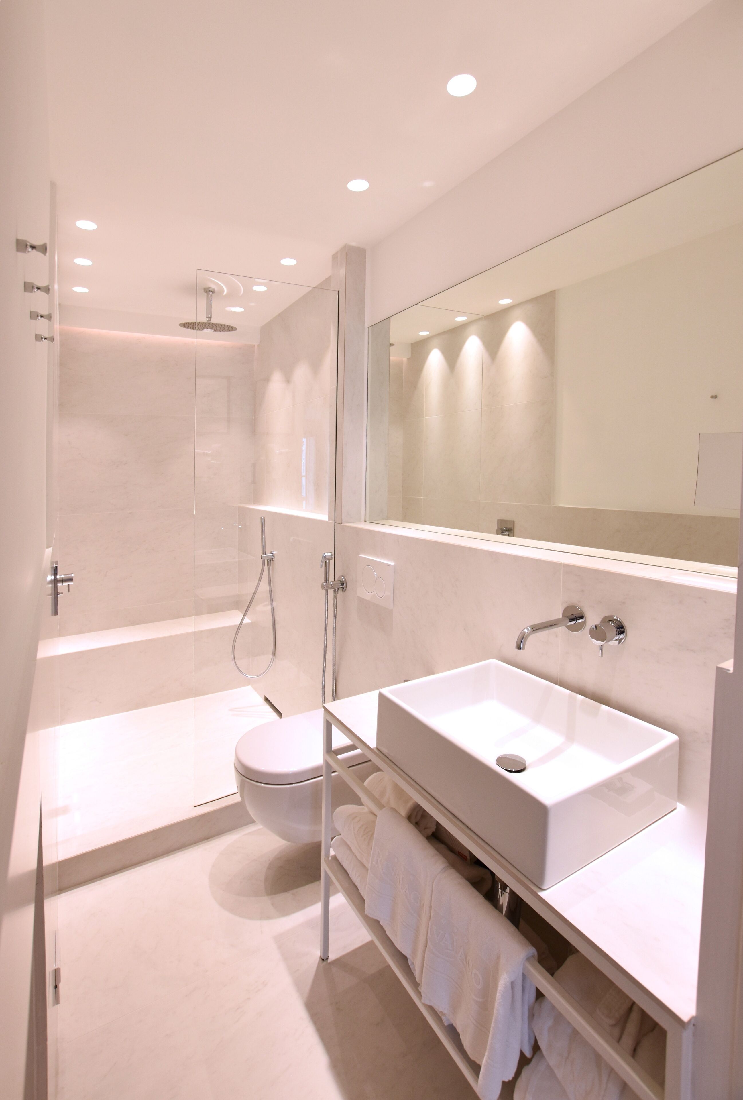 Un baño moderno con ducha envuelta en vidrio, un lavabo blanco y un espejo grande.