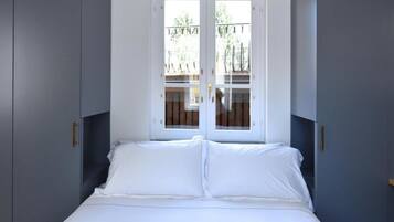 Un dormitorio con cama, ropa de cama blanca y ventana con vistas a un balcón.