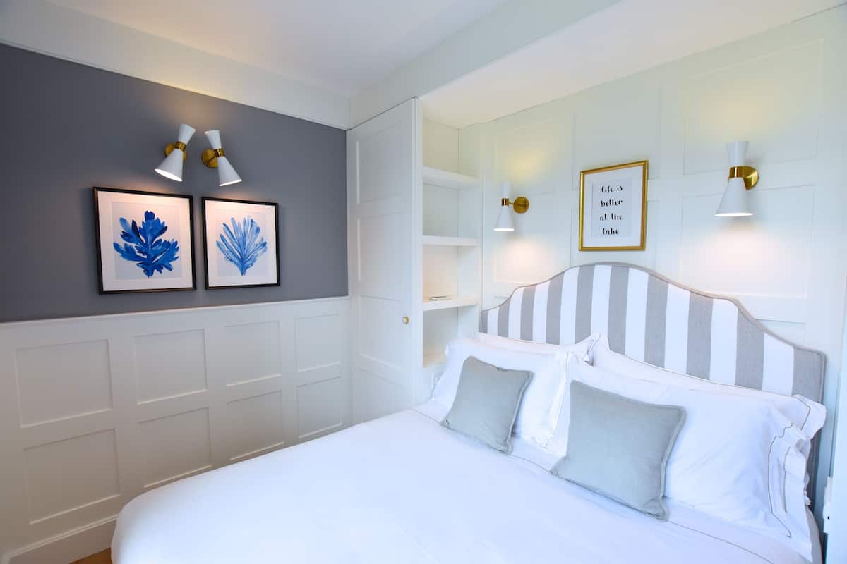 A neatly arranged bedroom with a large bed, white headboard, and two wall-mounted light fixtures.