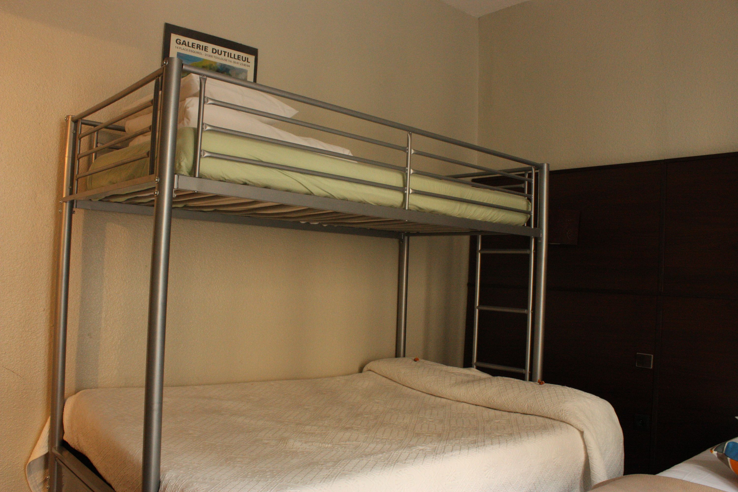 A bunk bed with a sign above it, a wooden wardrobe, and a wall-mounted shelf.