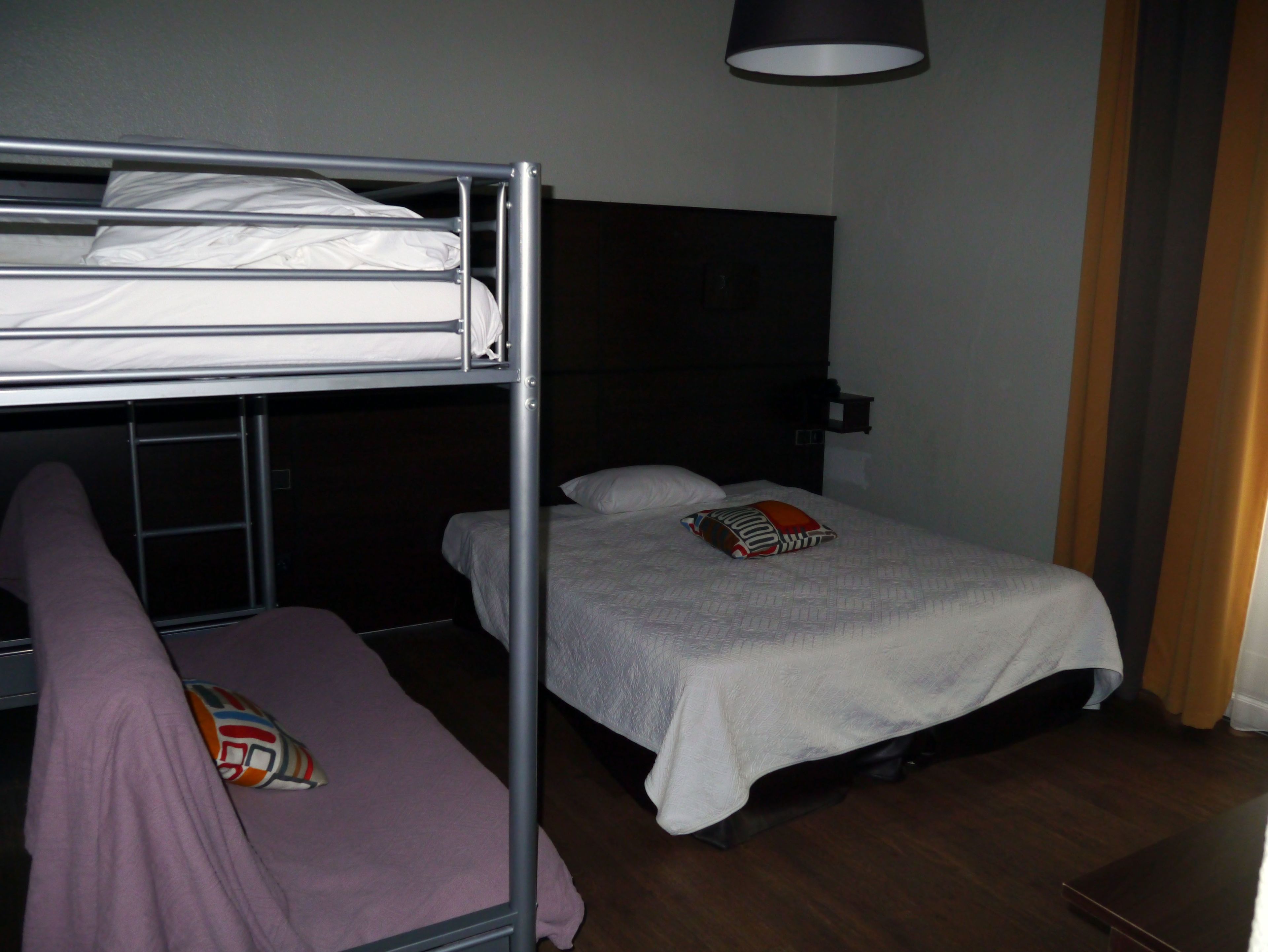 A room with a bunk bed, a single bed, and a bedside table.