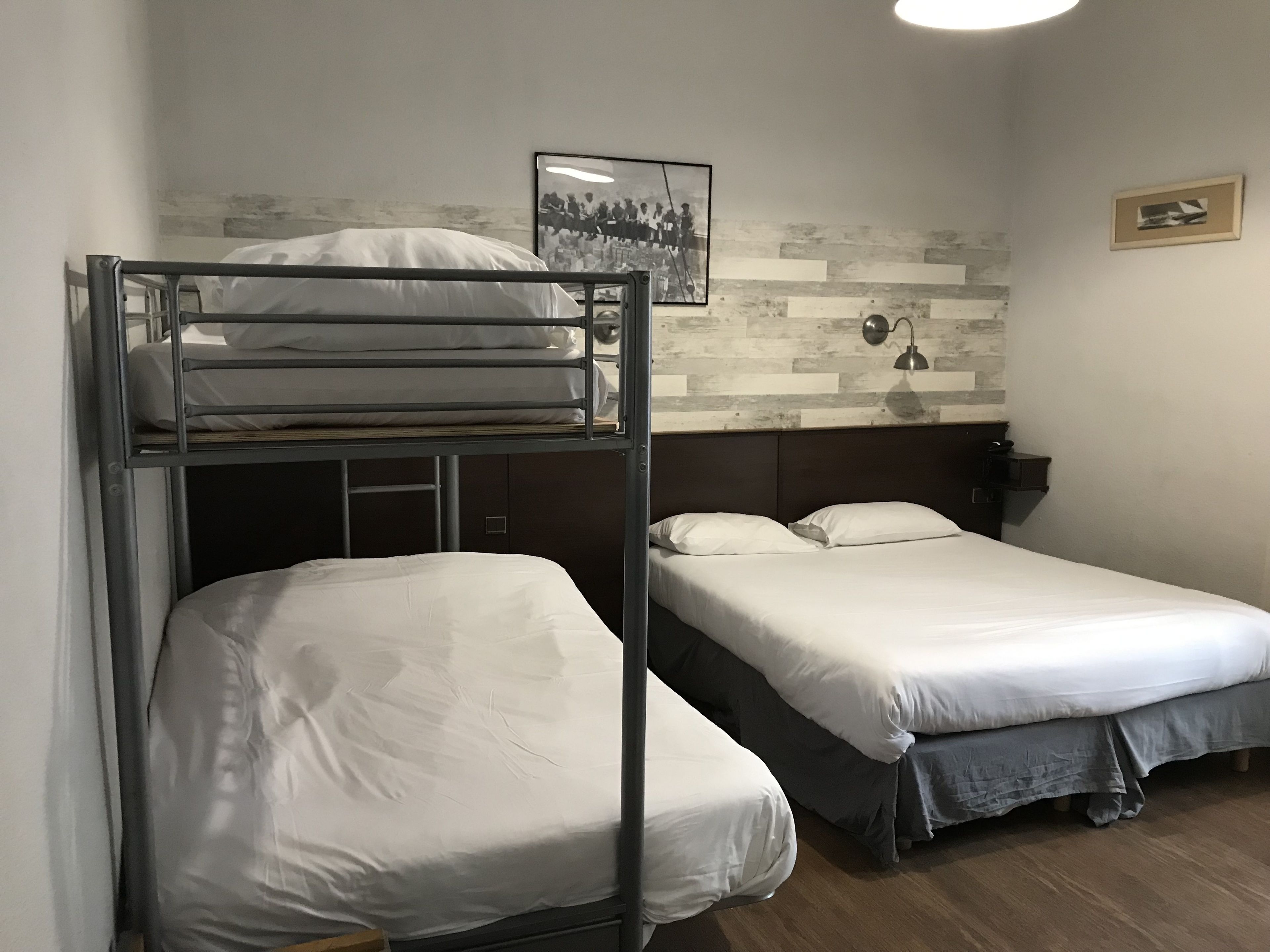 A room with two bunk beds, a wooden floor, a wall-mounted lamp, and a framed picture.