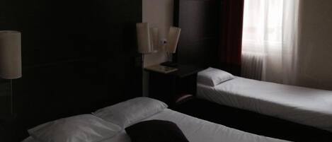 Habitación de hotel con dos camas individuales, una mesita de noche con lámpara y una ventana con cortinas.