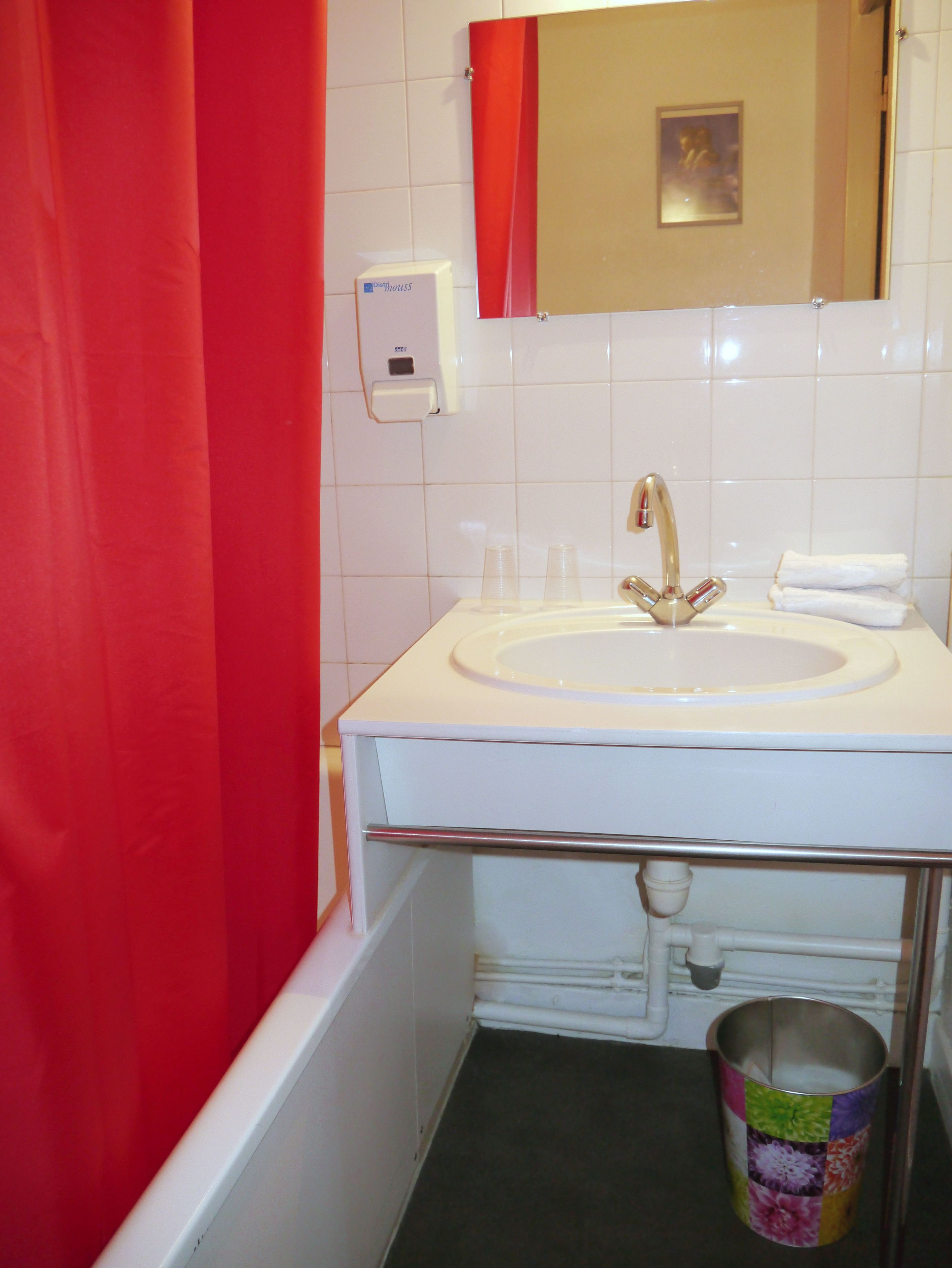 A bathroom with a white sink, a red shower curtain, a mirror, and a trash can.