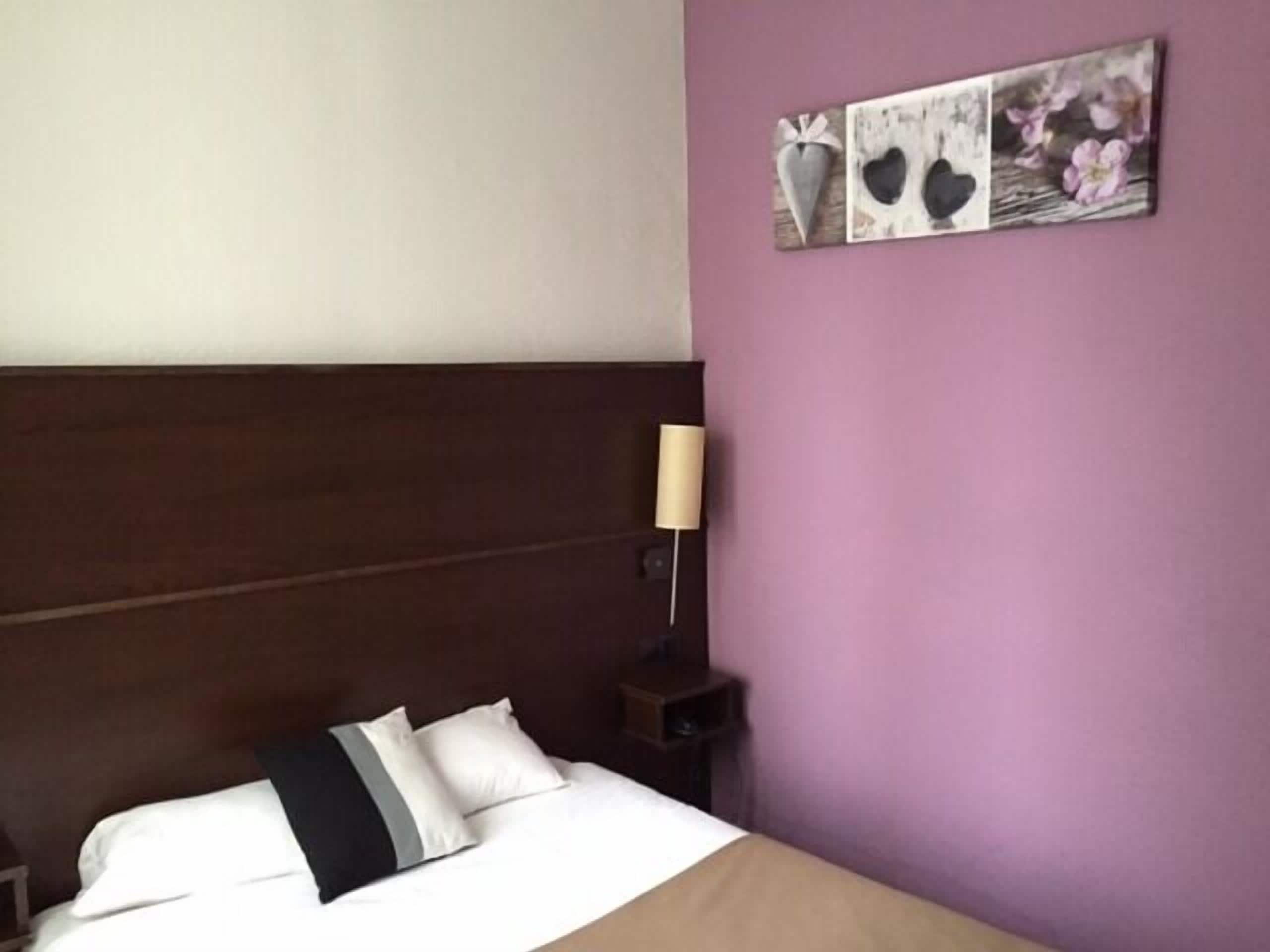 A hotel room with a bed, a nightstand, and a lamp.