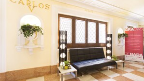 A lobby with a black leather sofa, a small table with a plant, and a sign that reads "CARLOS V CUARTO". - Hotel Carlos V (Granada)