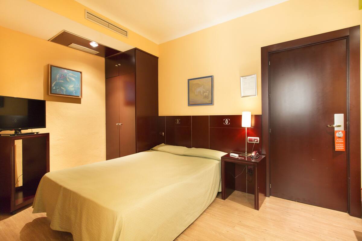 A hotel room with a bed, a television, a desk, and a door.