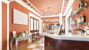 A hotel lobby with a checkered floor, a reception desk, a chandelier, and a wall with shelves of bottles. - Hotel Carlos V (Granada)