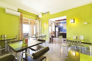 Habitación luminosa con paredes verdes, una mesa de vidrio y sillas. Hay una puerta que conduce a otra habitación.