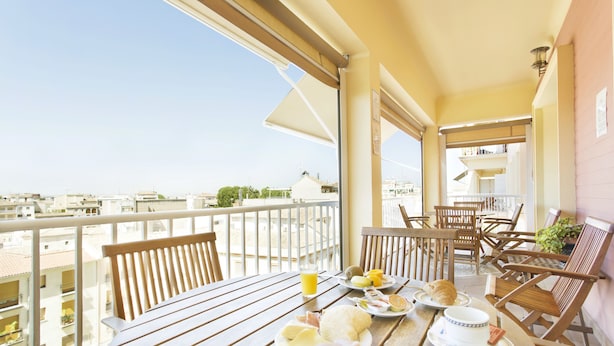 A balcony with a table set for breakfast, including plates with food and drinks, wooden chairs, and a view of the cityscape. - Hotel Carlos V (Granada)