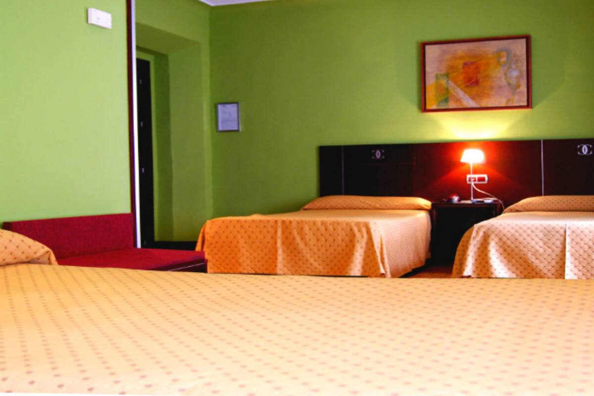 A hotel room with two beds, a red sofa, a nightstand with a lamp, and a painting on the wall.