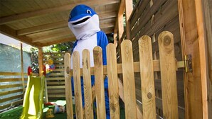 A wooden fence with a person in a blue and white costume partially obscured behind it. - Hotel Miramare (Mondolfo)