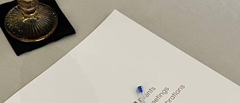A white paper with 'Castell' and 'Events Meetings Celebrations' text, a pen, and a golden glass on a black coaster.