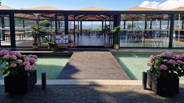 A covered outdoor dining area with tables and chairs, a wooden deck, and a view of the landscape. - Hotel El Castell (Sant Boi de Llobregat)