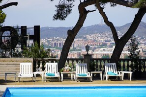A poolside area with white chairs and a view of a cityscape. - Hotel El Castell (Sant Boi de Llobregat)