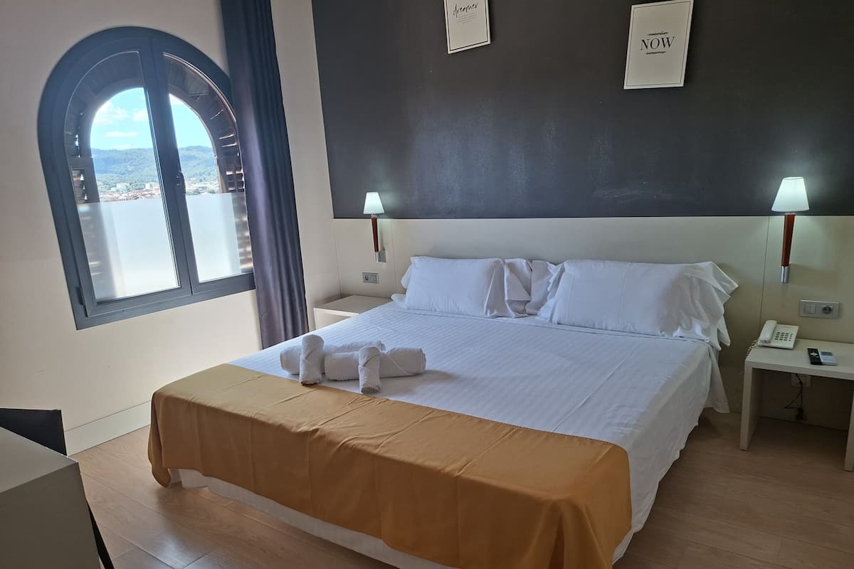 A hotel room with a bed, two bedside tables, a window with a view, and a wall with framed text.