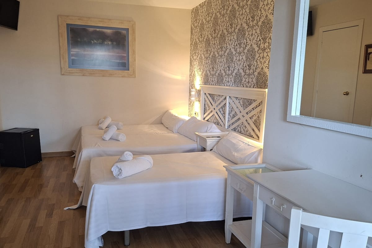 A hotel room with three beds, a desk, a mirror, a speaker, and a framed picture on the wall.
