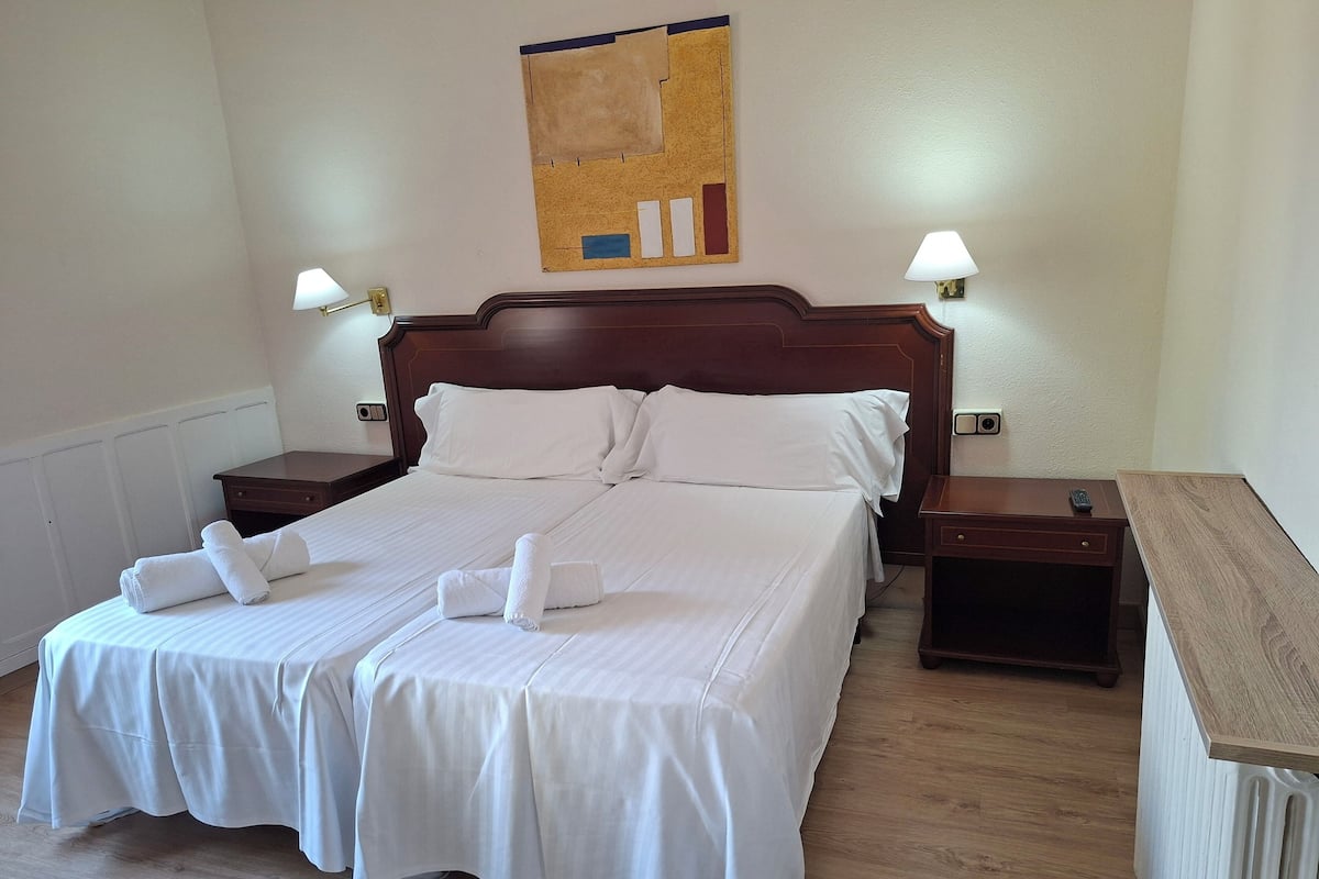 A neatly made double bed with white linens, two bedside tables with lamps, and a wooden headboard.