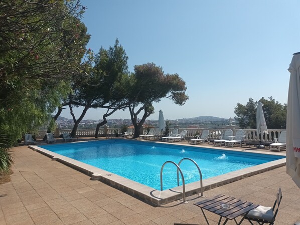 A swimming pool with a view of a cityscape, surrounded by trees and outdoor seating. - Hotel El Castell (Sant Boi de Llobregat)