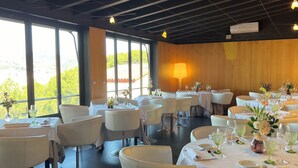 A restaurant with round tables, white chairs, and a view of greenery through large windows. - Hotel El Castell (Sant Boi de Llobregat)