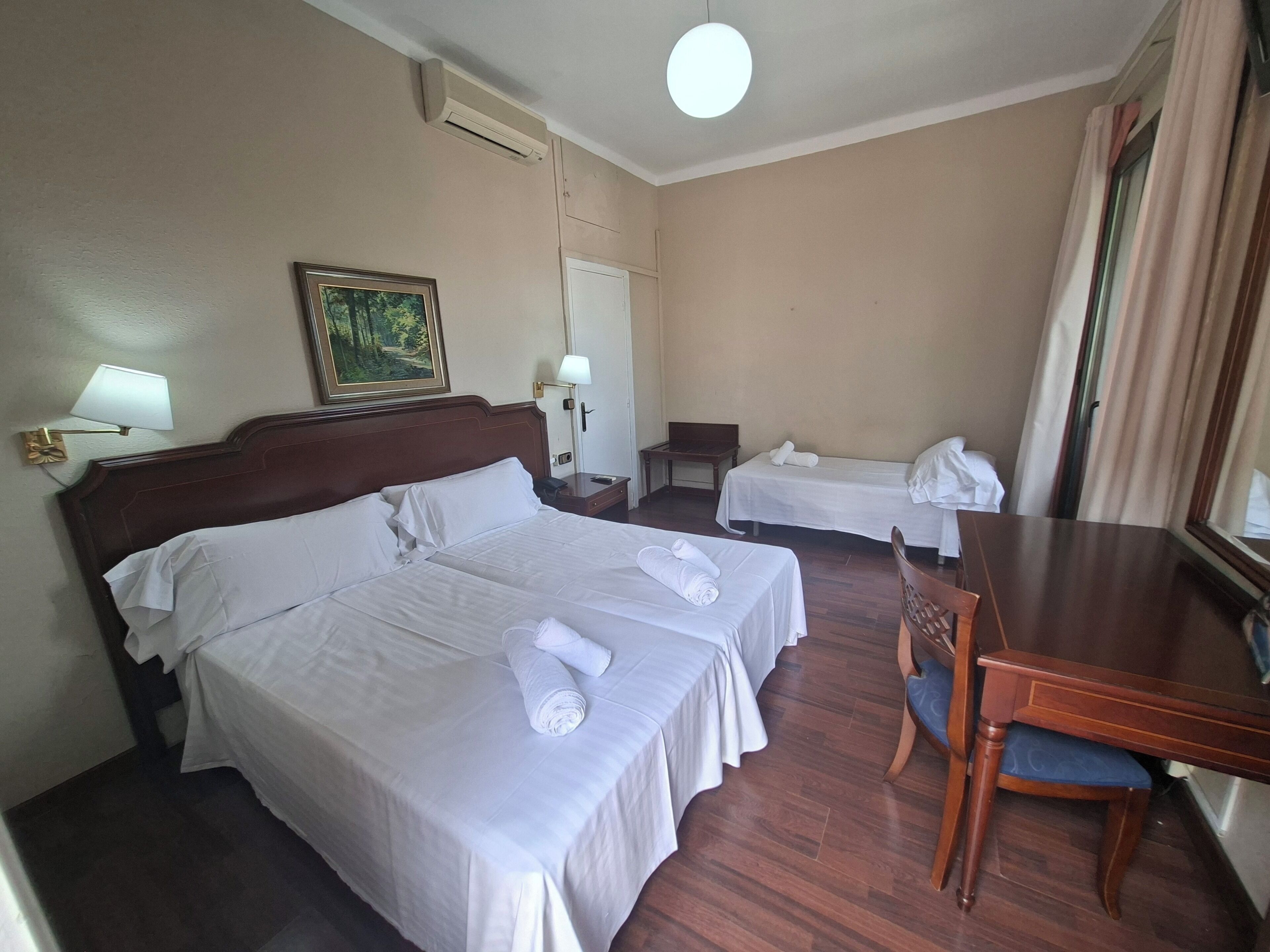 Habitación de hotel con dos camas, un escritorio, una silla, una lámpara, un cuadro y un equipo de aire acondicionado.