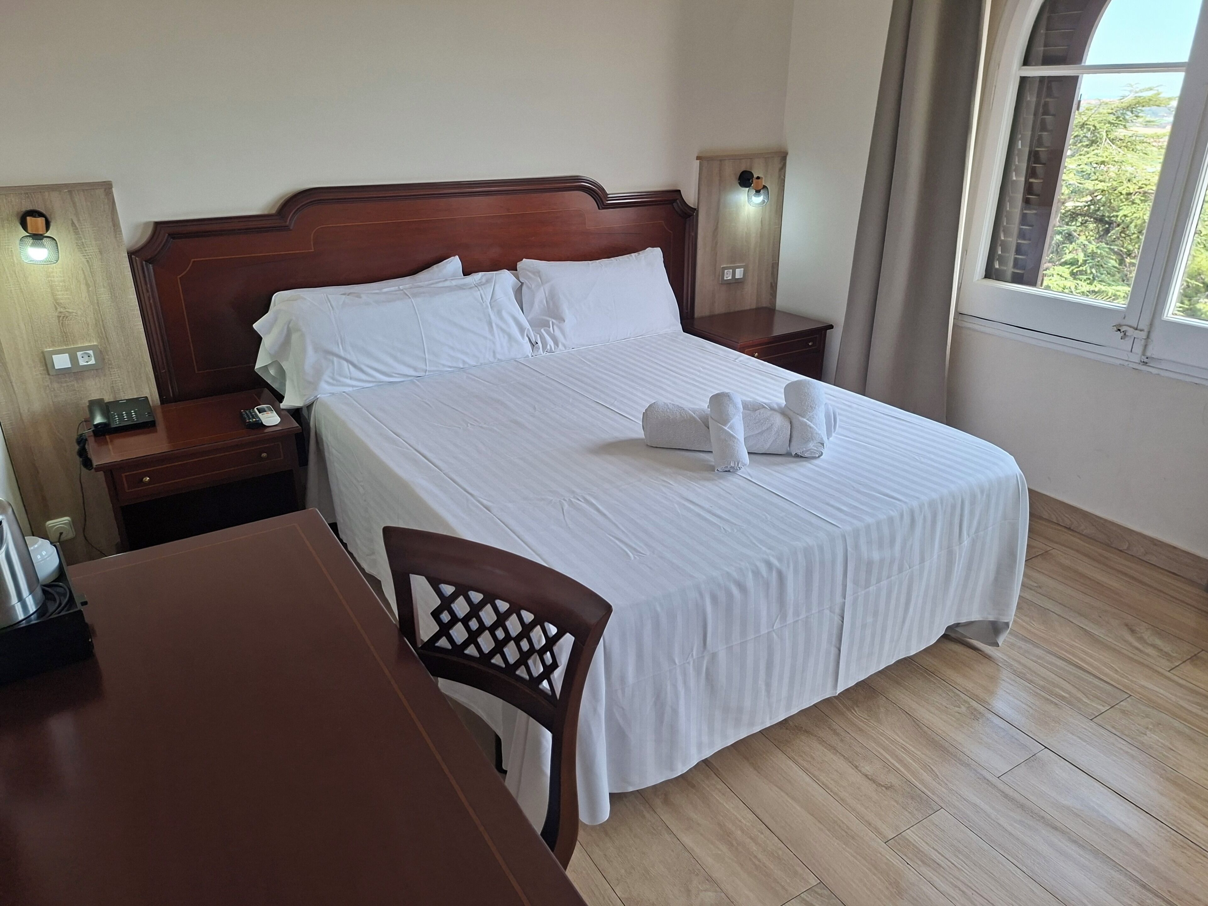 Une chambre d’hôtel avec un lit en bois, du linge de lit blanc, un bureau et une chaise.