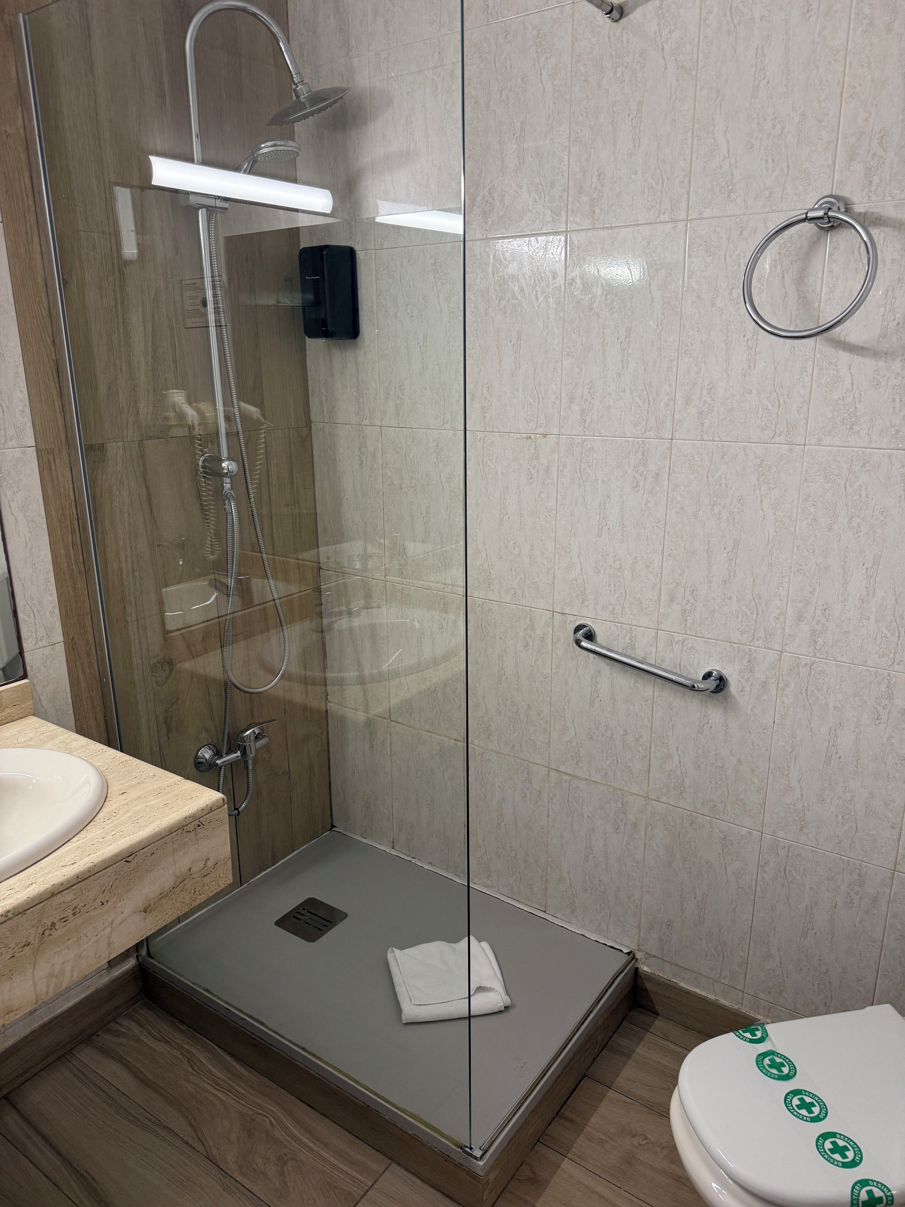 A bathroom with a glass-enclosed shower, a toilet with green stickers, and a sink.