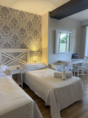 A hotel room with two beds, a desk, a chair, a mirror, and a patterned wallpaper. - Hotel El Castell (Sant Boi de Llobregat)