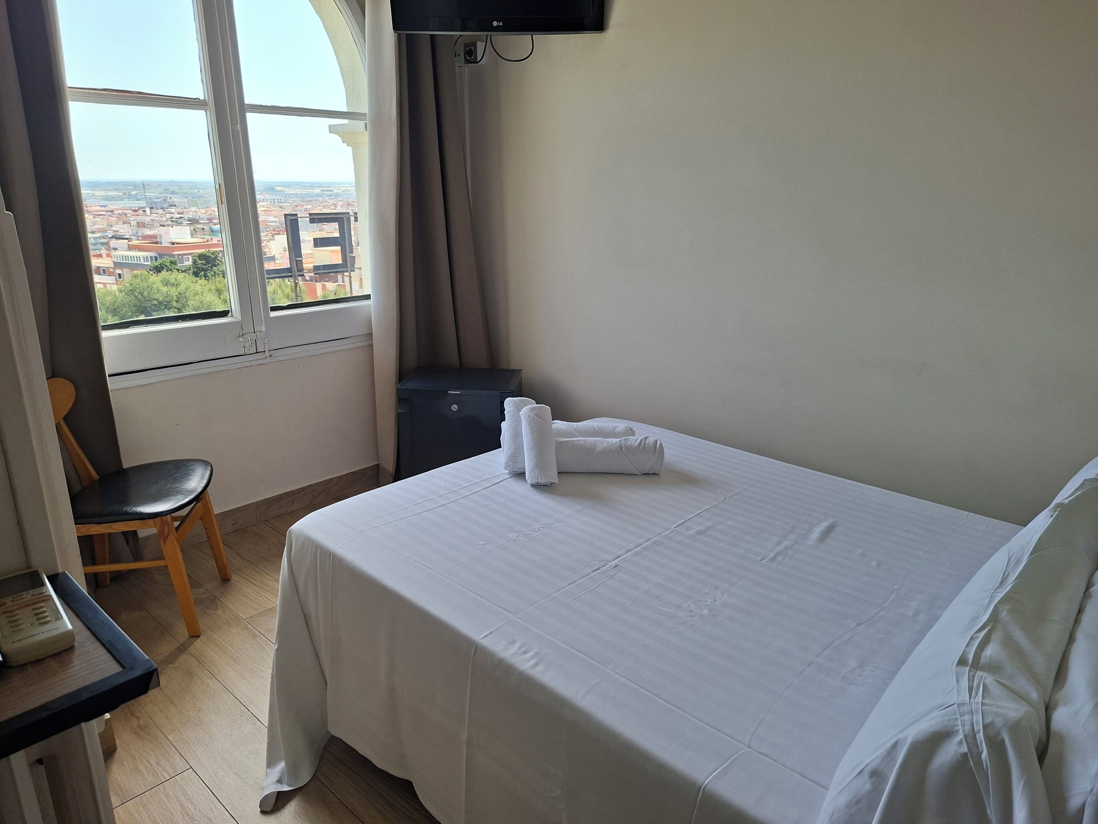 Ein Hotelzimmer mit Bett, Schreibtisch, Stuhl, Fernseher und einem Fenster mit Blick auf Gebäude.