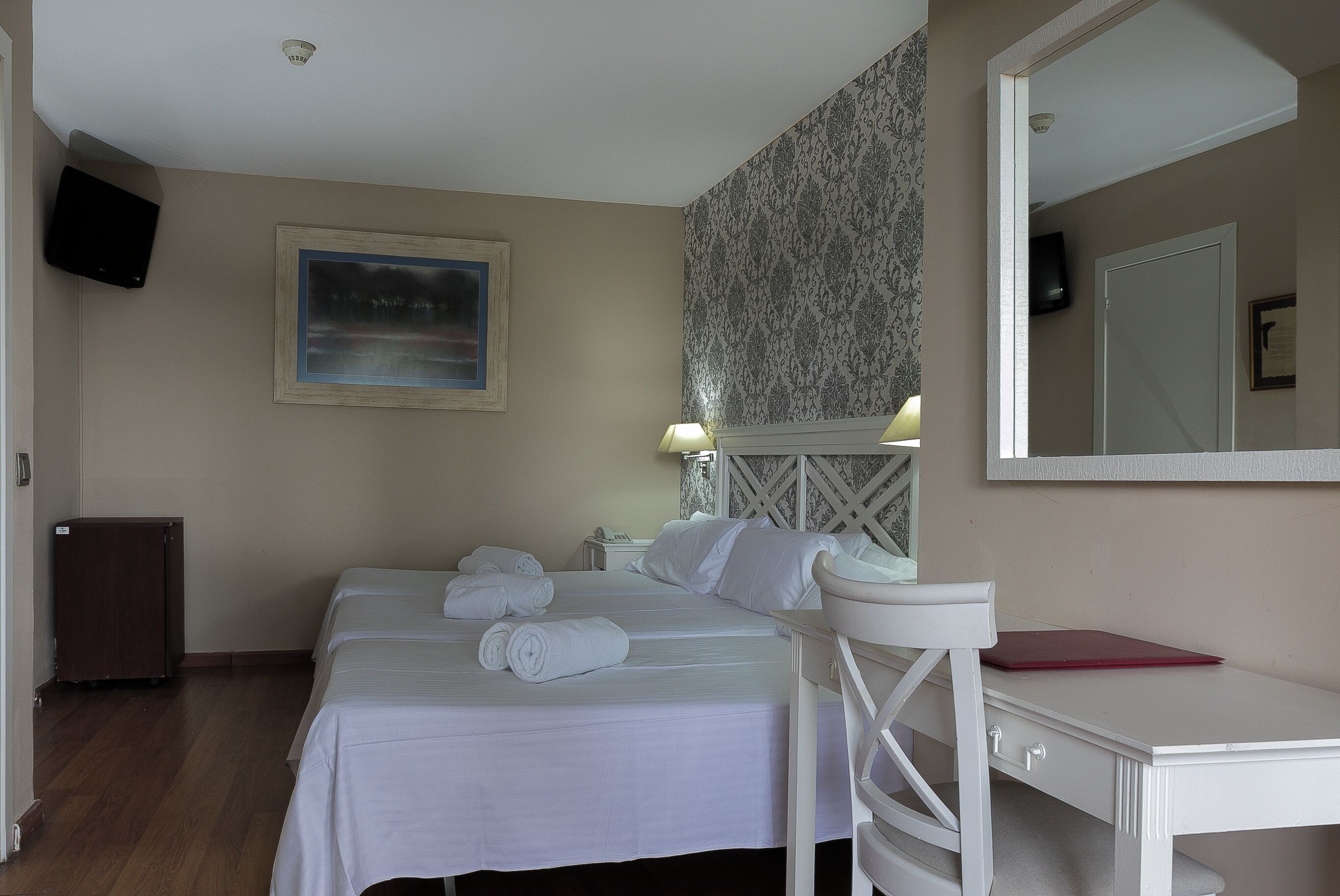 Habitación de hotel con dos camas, un escritorio, una silla, un televisor y un cuadro en la pared.