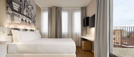 A modern hotel room with a large bed, a desk, a flat-screen TV, and a balcony with a city view.