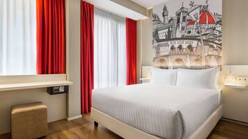 A hotel room with a large bed, a bedside table, a red and white curtain, a wall-mounted control panel, and a cityscape mural.