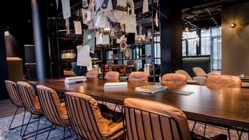 A modern conference room with a long table, leather chairs, and a hanging display of papers and sketches.