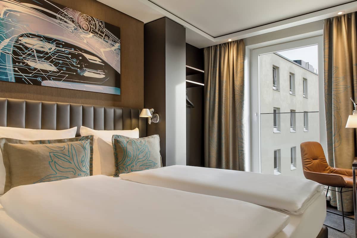 A hotel room with two beds, a modern headboard, a large window with curtains, and a city view.