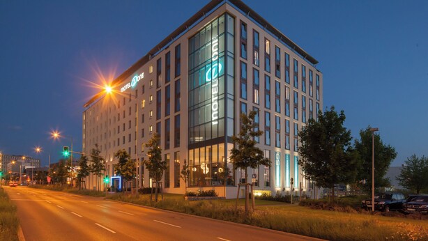 A modern hotel building with a prominent glass facade and a neon sign.