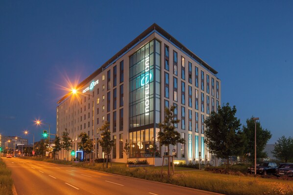 A modern hotel building with a prominent glass facade and a neon sign.