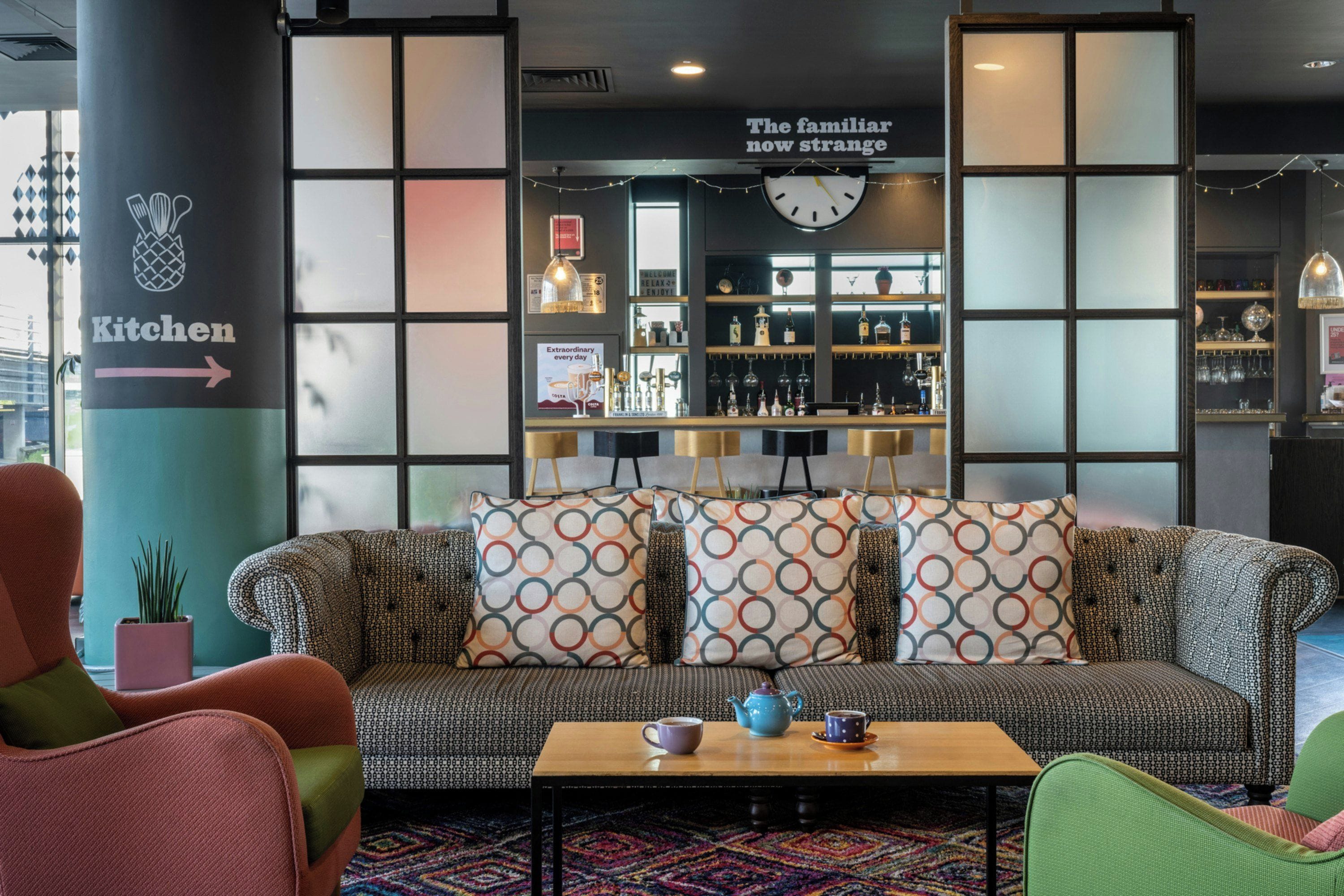 A modern lounge area with a sofa, chairs, a coffee table, and a bar area with shelves of bottles and glasses.