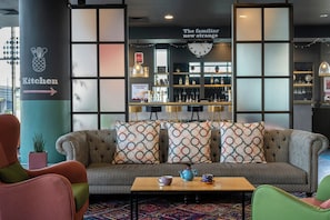 A modern lounge area with a sofa, chairs, a coffee table, and a bar area with shelves of bottles and glasses. - Leonardo Hotel Brighton (Brighton)
