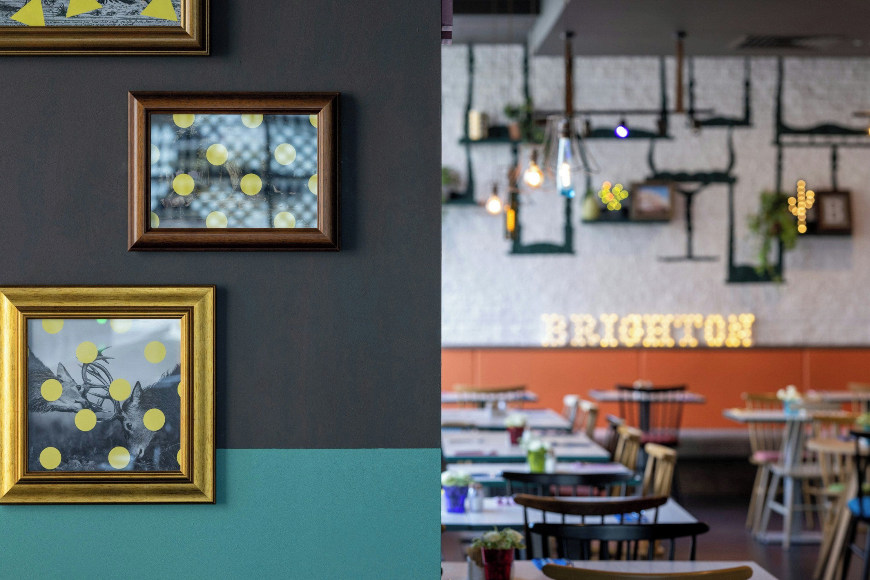 A restaurant interior with framed artwork on the wall, tables, chairs, and hanging lights.