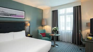 A hotel room with a bed, a chair, a table with a vase of flowers, a lamp, and a television.