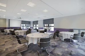 A conference room with multiple round tables, each surrounded by chairs. The room has a carpeted floor and large windows allowing natural light. - Leonardo Hotel Brighton (Brighton)