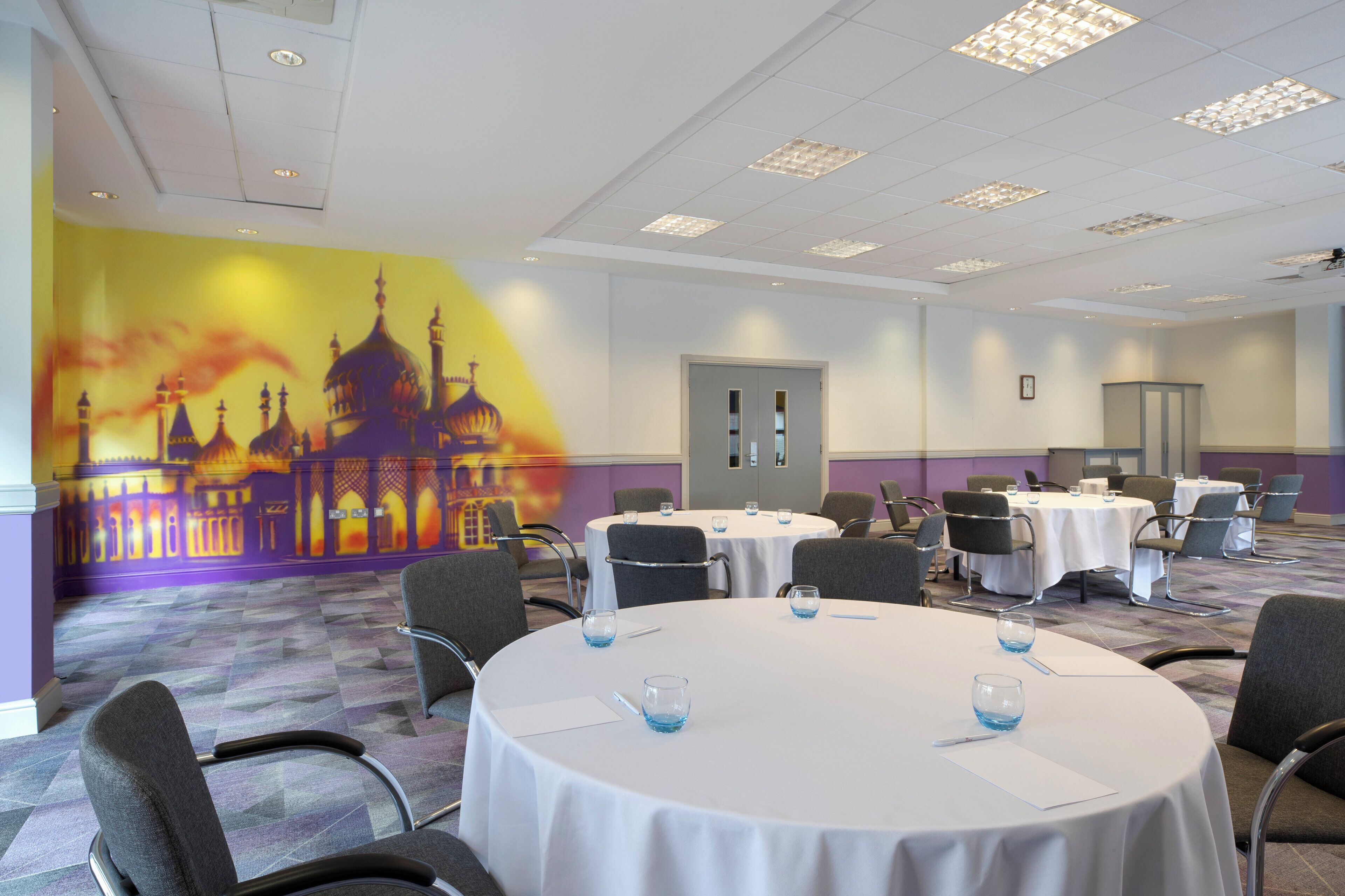 Un salón de conferencias con mesas redondas, sillas y un mural de un edificio en la pared.